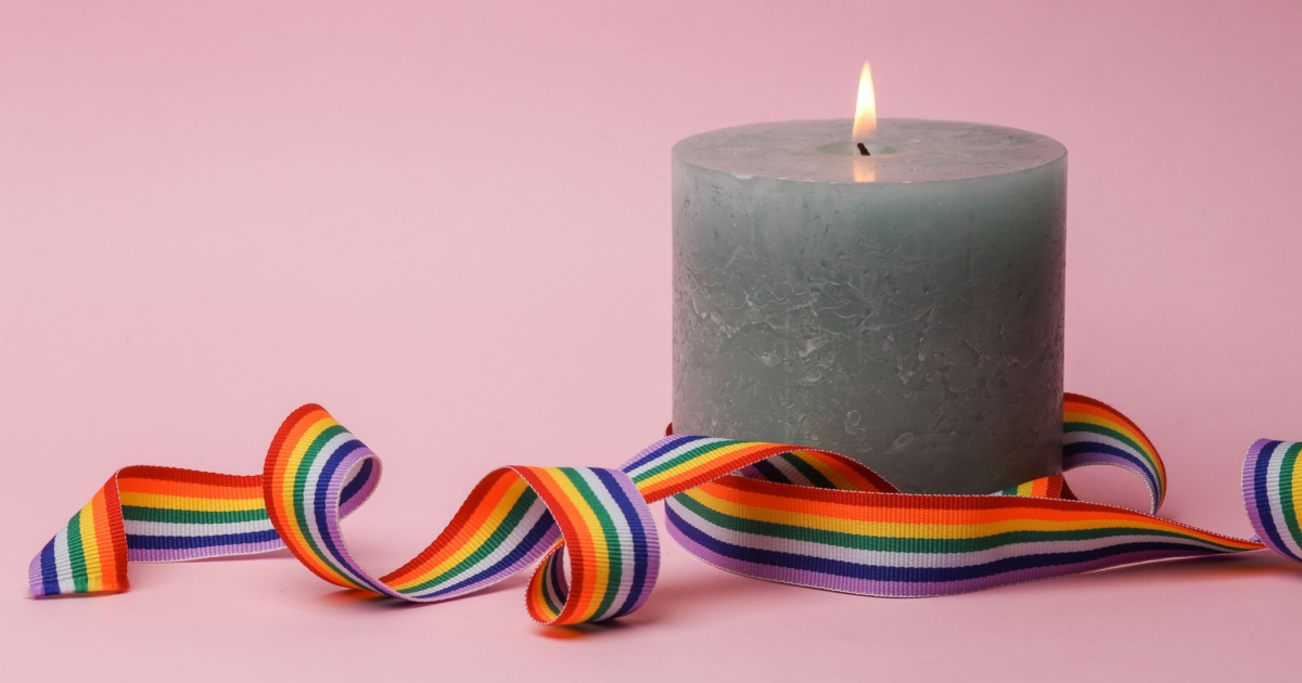 Image of rainbow ribbon next to grey candle on a pink background